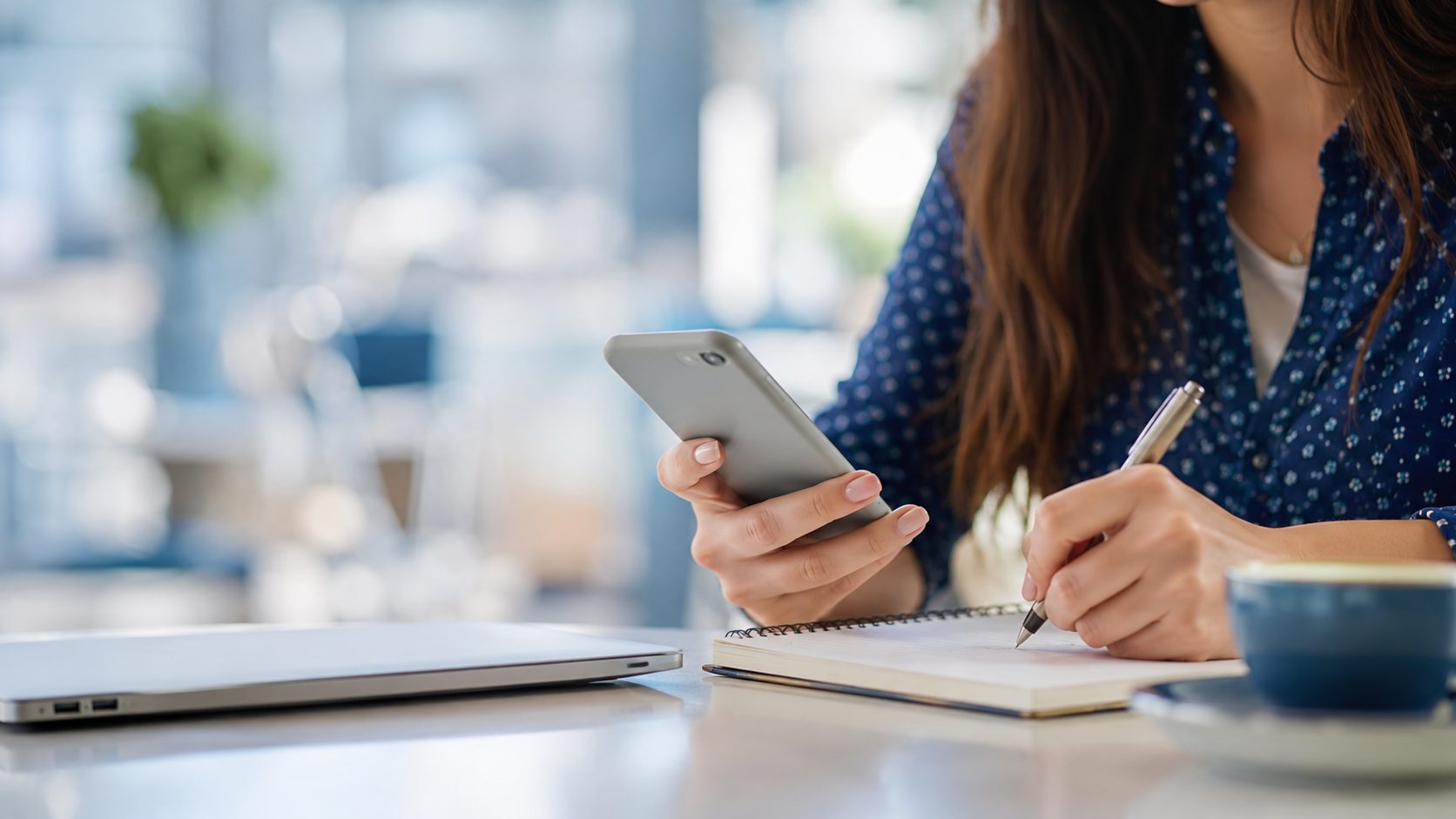 Mujer tomando notas junto a su teléfono móvil